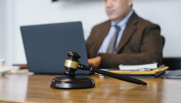 Crop concentrated Asian male judge in formal clothes sitting using modern netbook while working in law office