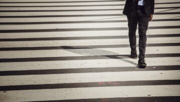 Faceless businessman with smartphone walking on crosswalk in sunlight