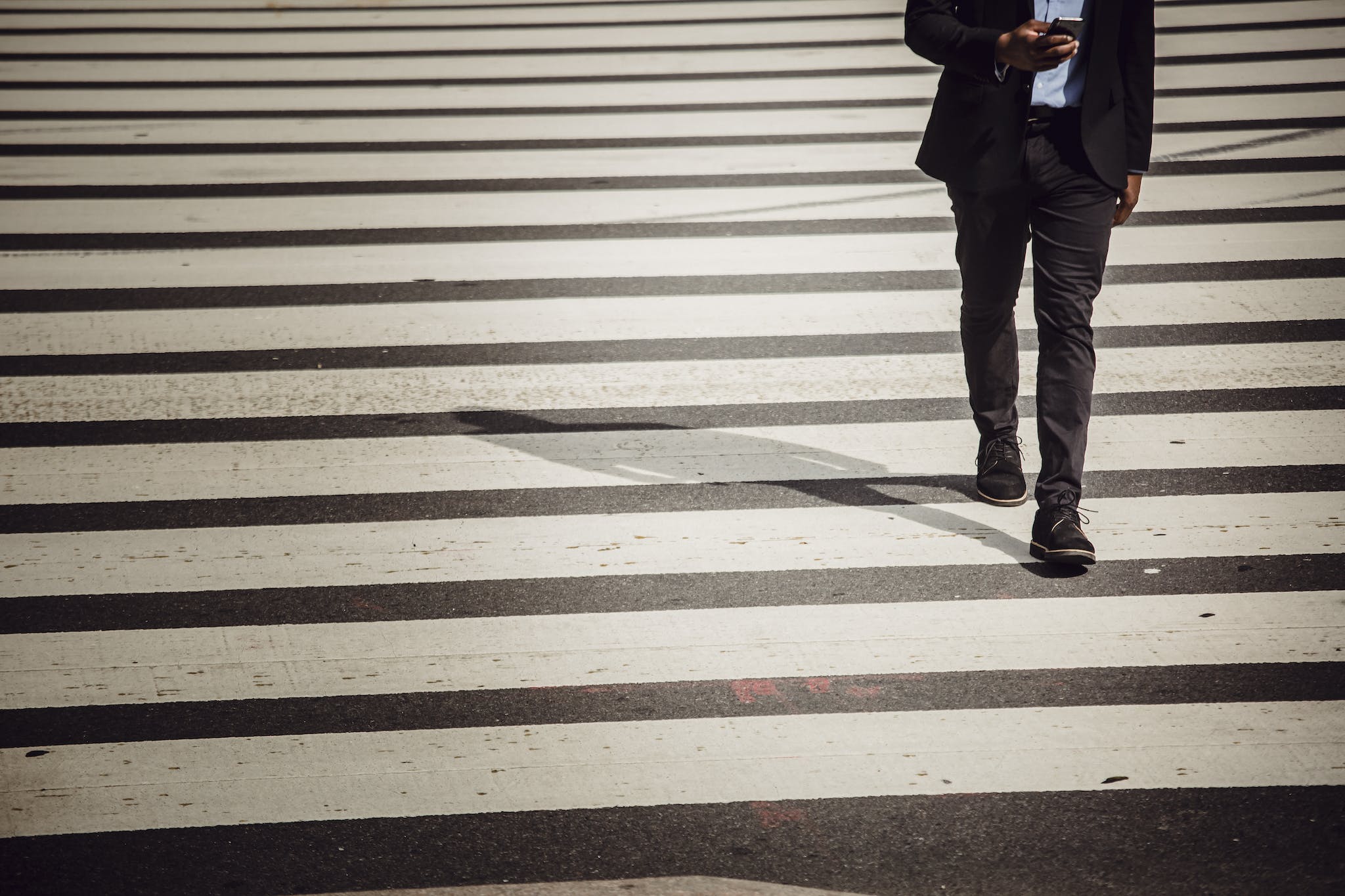 Faceless businessman with smartphone walking on crosswalk in sunlight