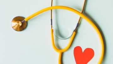 Medical stethoscope with red paper heart on white surface